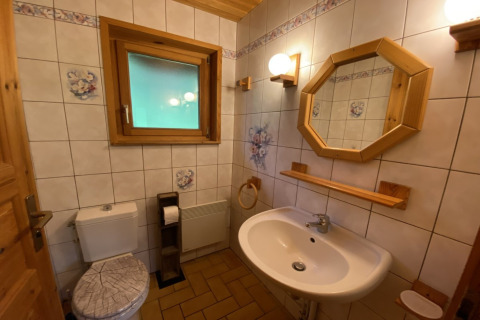Badkamer in een houten chalet met wit sanitair, bloemen tegels en houten accenten in Frankrijk.