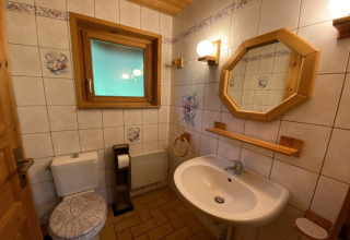 Bathroom inside a wooden chalet with white fixtures, floral tiles, mirror and wood accents in France.