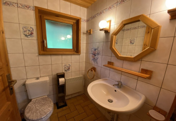 Badkamer in een houten chalet met witte sanitaire voorzieningen, bloemtegels en houtaccenten in Frankrijk.