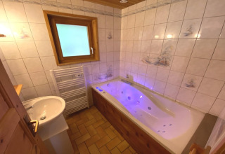 Bathroom with jacuzzi tub, tiled walls, wooden details, and a window in Le Fishing Lodge chalet, France.