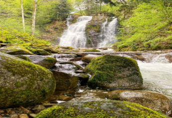 Foto eines Wasserfalls mit moosbedeckten Steinen, aufgenommen am Chalet 'Ronds Chetys' in Frankreich.