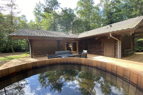 Wooden chalet in France with Nordic bath on timber deck, surrounded by lush forest and outdoor seating.
