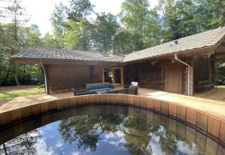 Houten chalet in Frankrijk met Scandinavisch bad op houten terras, omringd door bos en tuinmeubilair.