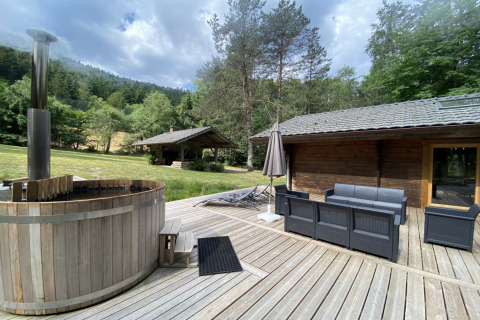 Buitenterras bij LE FISHING LODGE in Frankrijk met nordisch bad, zitmeubilair en groene omgeving.
