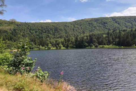 Vista su un lago tranquillo e colline verdi vicino allo chalet 'Ronds Chetys' in Francia in una giornata di sole.