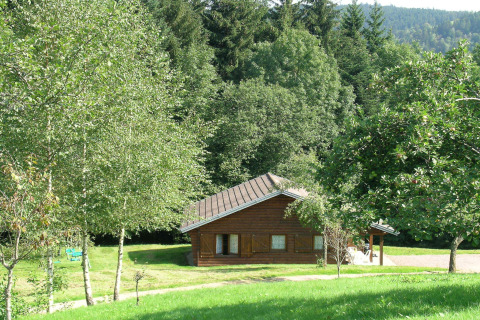 Chalet di legno 'Ronds Chetys' in Francia, circondato da alberi verdi e colline illuminate dal sole.