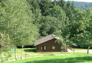 Chalet di legno 'Ronds Chetys' in Francia, circondato da alberi verdi e colline illuminate dal sole.
