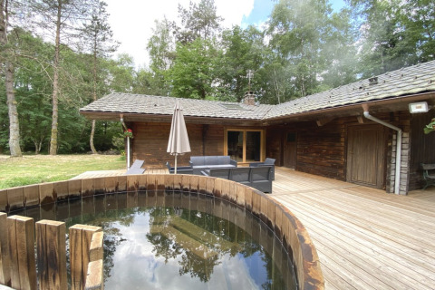 Houten chalet in Frankrijk met een ronde Scandinavische badkuip op een houten terras in het bos.