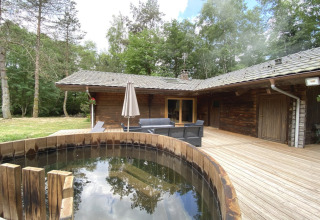 Houten chalet in Frankrijk met een ronde Scandinavische badkuip op een houten terras in het bos.