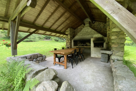 Zona pranzo esterna coperta con muri in pietra, barbecue, tavolo e sedie presso uno chalet in Francia.