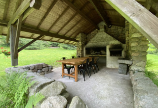 Covered outdoor dining area with stone walls, barbecue, wooden table and chairs at a chalet in France.