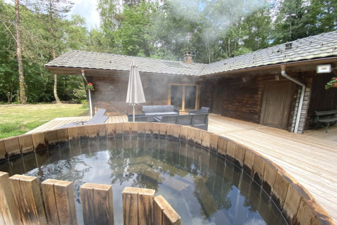 Houten chalet in Frankrijk met een Noordse bad op het terras, omringd door bos en buitenmeubilair.