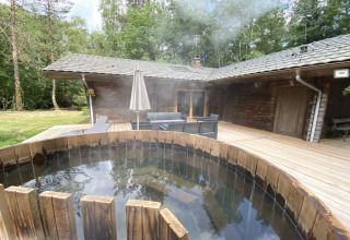 Houten chalet in Frankrijk met een Noordse bad op het terras, omringd door bos en buitenmeubilair.