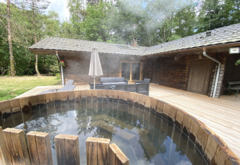 Houten chalet in Frankrijk met een Scandinavisch bad op het terras, omgeven door bos en tuinmeubelen.