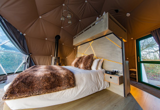 Modern bedroom with plush bedding, wood stove, and geometric windows in Chartwell Luxury Dome, UK.