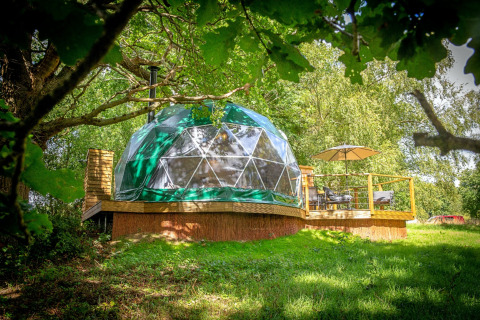 Chartwell Luxury Dome in het bos, met houten terras, parasol en zicht op een prachtig groene natuurlijke omgeving.