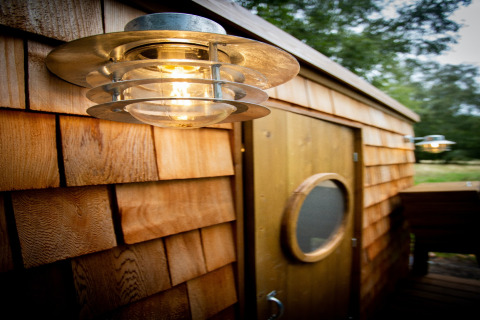 Outdoor lamp on the wooden shingle wall of Chartwell Luxury Dome, UK, beside a circular window door.