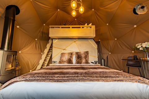 Elegant interior of Chartwell Luxury Dome featuring a cozy bed, wood stove, and lofted space in the United Kingdom.