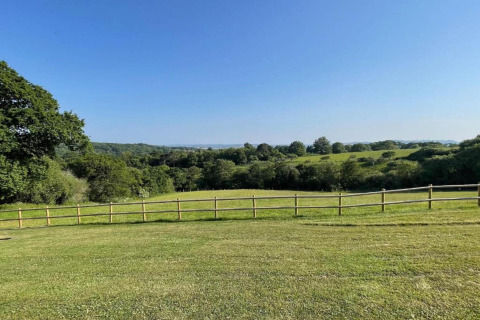 View from the dome overlooking open green fields, a wooden fence, and trees under a clear blue sky.