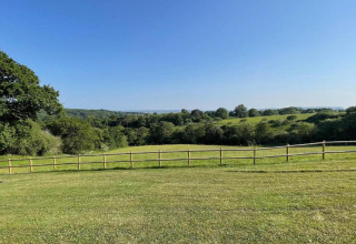 View from the dome overlooking open green fields, a wooden fence, and trees under a clear blue sky.