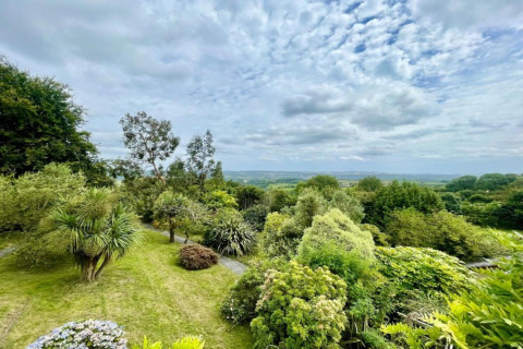 View from a dome overlooking lush green gardens and distant fields under a partly cloudy sky.