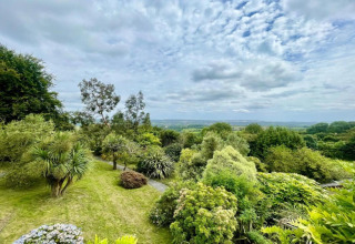 View from a dome overlooking lush green gardens and distant fields under a partly cloudy sky.