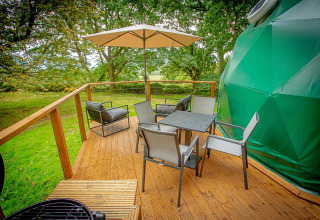 Udendørs terrasse ved Hever Luxury Dome i Storbritannien med stole, parasol og udsigt til træer.