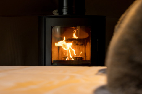En hyggelig pejs med flammer i Hever Luxury Dome, Storbritannien, set fra en seng i forgrunden.