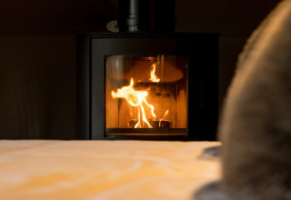 En hyggelig pejs med flammer i Hever Luxury Dome, Storbritannien, set fra en seng i forgrunden.