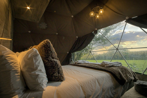 Hyggeligt soveværelse i Hever Luxury Dome, med stor seng, blødt tæppe og udsigt over grøn eng.