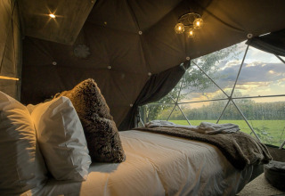 Hyggeligt soveværelse i Hever Luxury Dome, med stor seng, blødt tæppe og udsigt over grøn eng.