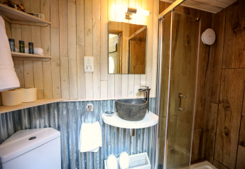 Badkamer in een koepel met houten wanden, glazen douche, stenen wastafel en rustieke planken.