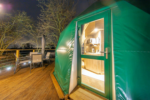 Udsigt til terrasse og indgang til Hever Luxury Dome i Storbritannien, oplyst om natten.