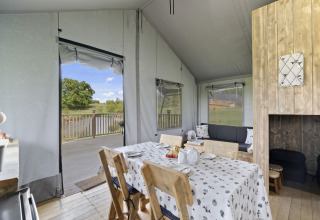 Interieur van The Herdwick Safari Tent in het VK, met eethoek, terras en uitzicht op bomen en water.