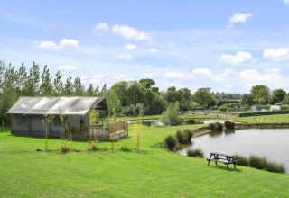 Het Herdwick Safari Tent naast een vijver met picknicktafel, op een groene weide in het Engelse platteland.