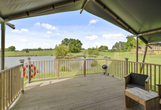 Uitzicht vanuit The Herdwick Safari Tent in het VK met houten terras, vijver en groene weiden.