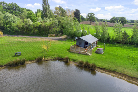 De Herdwick Safari Tent naast een vijver, omgeven door gras en bomen op het Britse platteland.