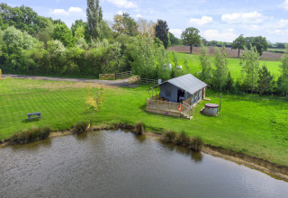 De Herdwick Safari Tent naast een vijver, omgeven door gras en bomen op het Britse platteland.