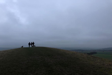 Silhouet van drie mensen en twee honden op een heuveltop onder een bewolkte lucht bij The Herdwick Safari Tent, VK.