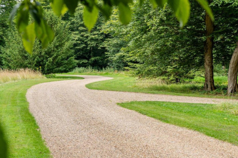 Kronkelend grindpad tussen groene bomen en gras bij een glamping-accommodatie in de natuur.
