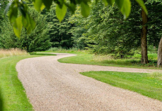 Kronkelend grindpad tussen groene bomen en gras bij een glamping-accommodatie in de natuur.