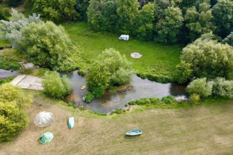 Luchtfoto van een glampinglocatie met tenten, bootjes en een caravan bij een rivier omringd door bomen.