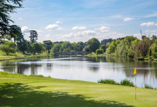 Foto van een golfbaan bij een meer omringd door bomen, gemaakt bij een glamping accommodatie.
