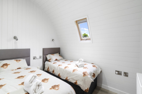 Sfeervolle tweepersoonskamer in The Highland Camping Pod met witte muren, twee bedden en dierenbeddengoed.