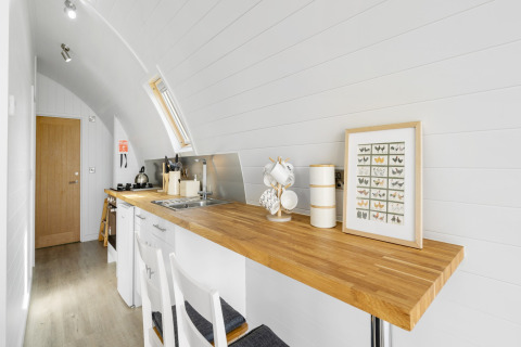 Moderne, lichte keukenhoek in The Highland Camping Pod met houten blad, wit interieur en vlinderkunstwerk.
