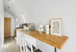 Moderne, lichte keukenhoek in The Highland Camping Pod met houten blad, wit interieur en vlinderkunstwerk.