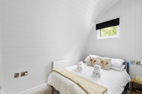 Lichte slaapkamer in The Highland Camping Pod, Verenigd Koninkrijk, met tweepersoonsbed en klein raam.