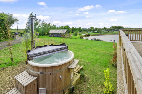 Uitzicht op houten hottub en meer bij The Highland Camping Pod in het VK, omringd door groen landschap.