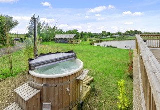 Uitzicht op houten hottub en meer bij The Highland Camping Pod in het VK, omringd door groen landschap.