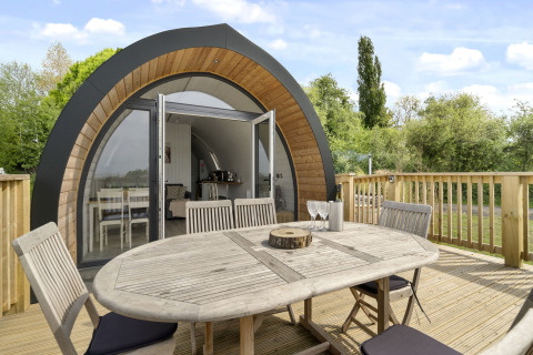 Buitenterras met tafel en stoelen voor The Highland Camping Pod, omringd door groene natuur.